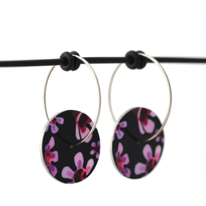 Circle earrings featuring pink Geraldton Wax flowers on a black background. The aluminium earrings discs are approximately 16mm in diameter and the surgical stainless steel hoop attachments are 20mm in diameter.