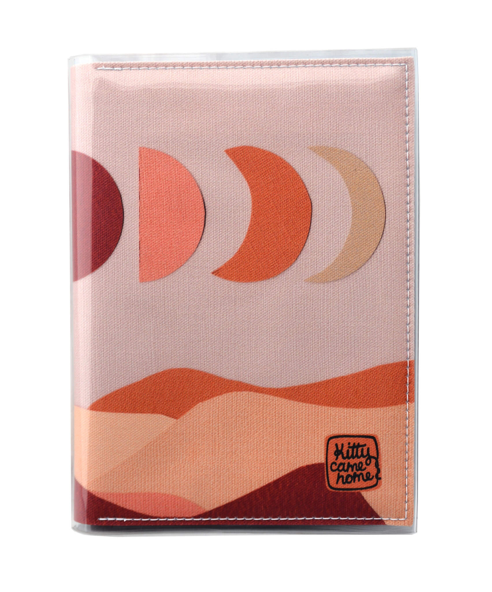 This is an image of the front of a Kitty Came Home A5 journal in the 'Moonshadow drive’ design by Satin and Tat. The moon appears in all its phases in a dusty pink sky above a landscape lit by the moon's colours: burgundy, oranges, and apricot.