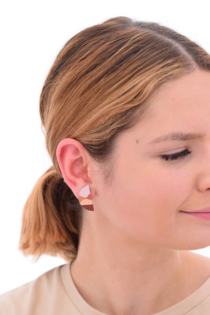This image shows a woman wearing a Kitty Came Home stud earring in her right ear. The semi circle shape is 25 millimetres in diameter. The design is called lily of the valley by Satin and Tat. A landscape of gently rolling hills in terracotta colours beneath a pale pink sky.