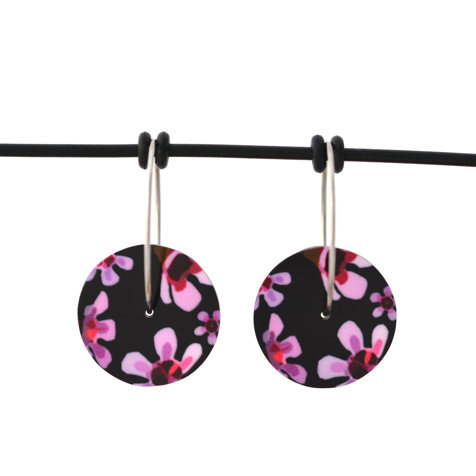 Circle earrings featuring pink Geraldton Wax flowers on a black background. The aluminium earrings discs are approximately 16mm in diameter and the surgical stainless steel hoop attachments are 20mm in diameter.