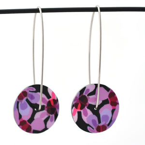Circle earrings featuring pink Geraldton Wax flowers on a black background. The aluminium earrings discs are approximately 26mm in diameter and the surgical stainless steel drop hooks are approximately 40mm in length.