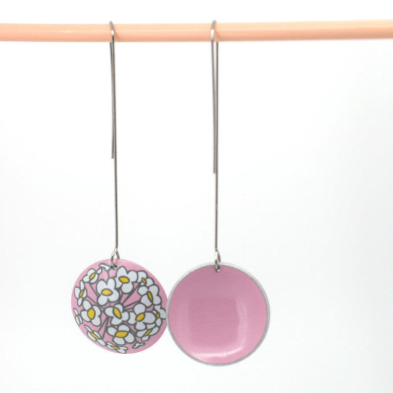 Photo of a pair of earrings showing both sides. The earrings are 26 millimetre in diameter domed circles on 50 millimetre long stainless steel hand formed hook. The earrings are aluminium and the printed design is a Sweet Alyssum flower on a soft pink background. The Sweet Alyssum design is printed on the convex side of the dome. The concave, reverse side is soft pink. 