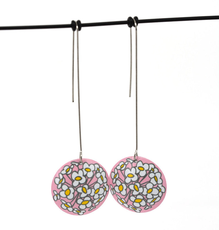 Photo of earrings. 26 millimetre diameter domed circle earrings on 50 millimetre long stainless steel hooks. The earrings are aluminium. The design is a interpretation of a Sweet Alyssum flower on a soft pink background. The design is printed on the convex side of the dome.