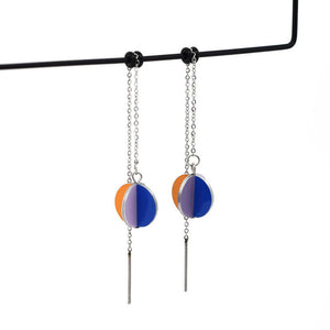 A photo of a pair of earrings hung on stainless steel earring threads. The earrings are approximately 13 millimetres in diameter. Each is a sphere formed from 4 folded pieces of aluminium. Printed on each of the 8 faces is one of four colours derived from a photo of a poesy of daisies. The soft pink and lilac of the petals; the rich egg-yolk yellow of the daisy's heart, and the blue of framing backdrop.