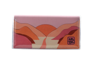 This is an image of the front of a Kitty Came Home bifold plus purse clutch in 'The Golden Dawn' design by Satin and Tat. A path wends through a valley of pink and orange hills towards a rising orange sun. This is the large size.