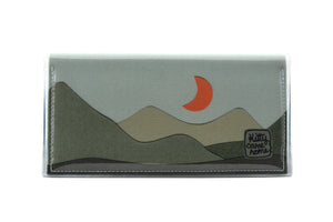 This is an image of the front of a Kitty Came Home bifold plus purse clutch of the 'Moondance' design by Satin and Tat. An orange crescent moon floats above a landscape of dark green hills. This is the large size.