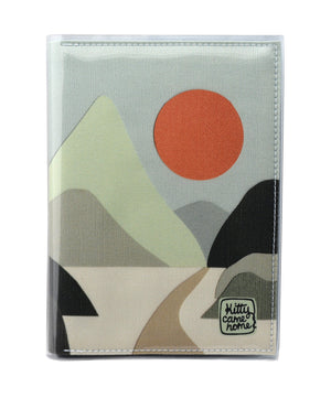 This is an image of the front of a Kitty Came Home A5 journal in the 'Moonlight drive' design by Satin and Tat. An orange moon in a pale green sky above a landscape of green hued hills. A path leads between the hills toward the distant mountains.