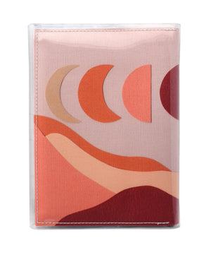 This is an image of the rear of a Kitty Came Home A5 journal in the 'Moonshadow drive’ design by Satin and Tat. The moon appears in all its phases in a dusty pink sky above a landscape lit by the moon's colours: burgundy, oranges, and apricot.