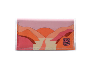 This is an image of the front of a Kitty Came Home bifold mini purse clutch in 'The golden dawn' design by Satin and Tat. A path wends through a valley of pink and orange hills towards an orange rising sun. This is the small size.