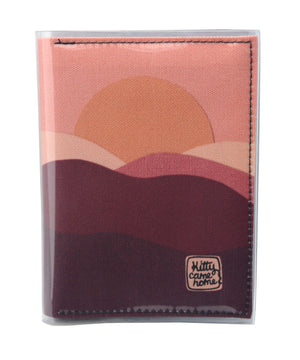 This is an image of the front of a Kitty Came Home A6 journal in 'The night comes down' design by Satin and Tat. An orange sun in a pink sky sinks behind a pink and magenta landscape of rolling hills.