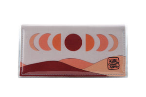 This is an image of the front of a Kitty Came Home bifold plus purse clutch in 'The same moon shines' design by Satin and Tat. The moon appears in all its phases in a white sky above a landscape lit by the moon's colours: burgundy, oranges, and apricot. This is the large size.