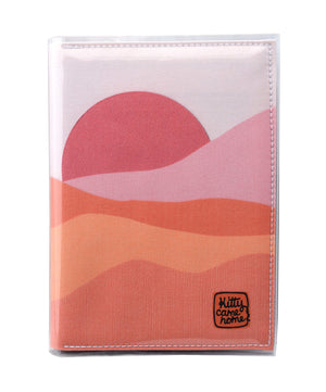 This is an image of the front of a Kitty Came Home A5 journal in the 'Waiting for the sun' design by Satin and Tat. A warm pink sun rises over a landscape of pink hued sands.